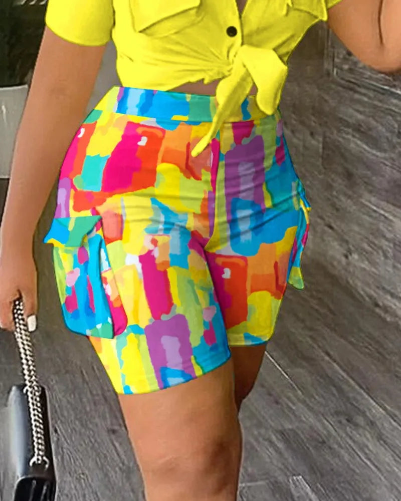 Woman wearing colorful abstract print summer shorts with side pockets and a yellow short-sleeve tied crop top