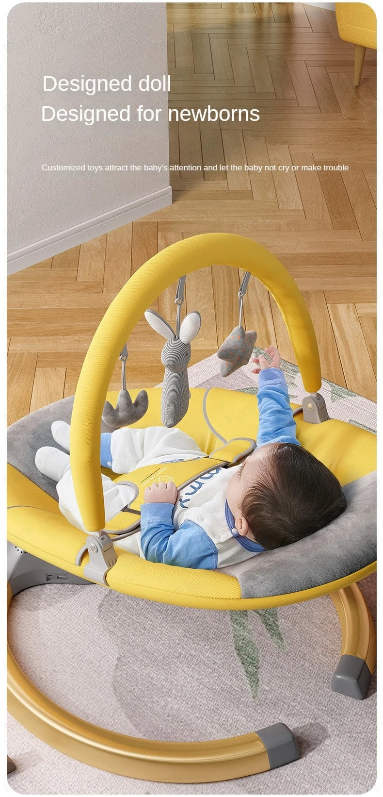 Baby lying in a yellow and gray electric rocking chair reaching for hanging soft toys indoors on a wooden floor