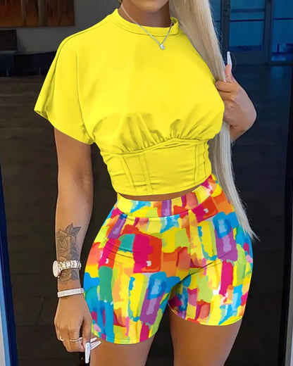 Woman wearing vibrant two-piece summer outfit with a yellow fitted crop top and colorful abstract print shorts