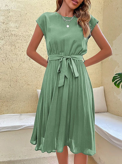 Elegant green summer beach dress for women with pleated skirt and waist tie, styled indoors with casual vibe