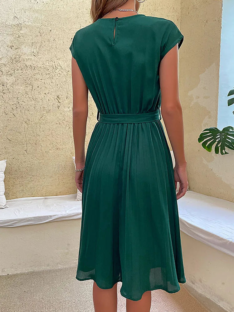 Woman wearing elegant dark green pleated summer beach dress with belt viewed from the back indoors