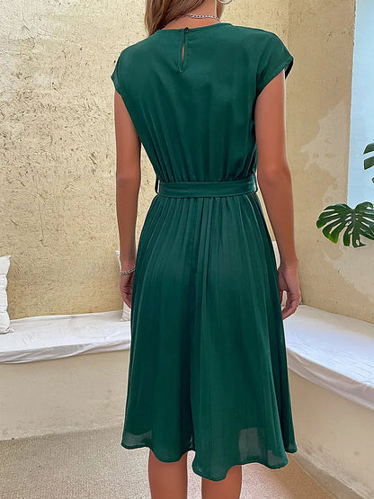 Woman wearing elegant dark green pleated summer beach dress with belt viewed from the back indoors
