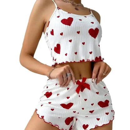 Woman wearing a two-piece white pajama set with red heart print, cropped camisole, and matching shorts with bow detail