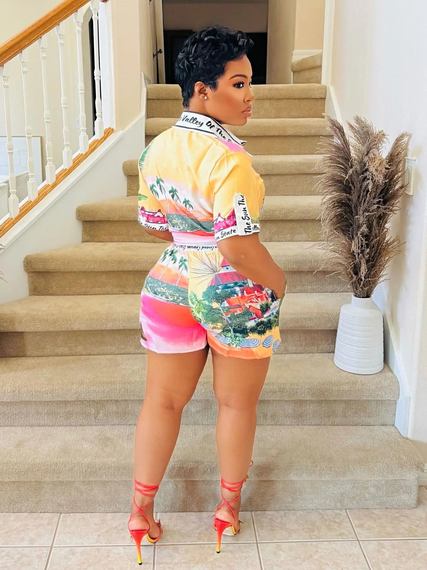 Woman wearing a colorful two-piece summer outfit with short-sleeve top and matching shorts standing on stairs