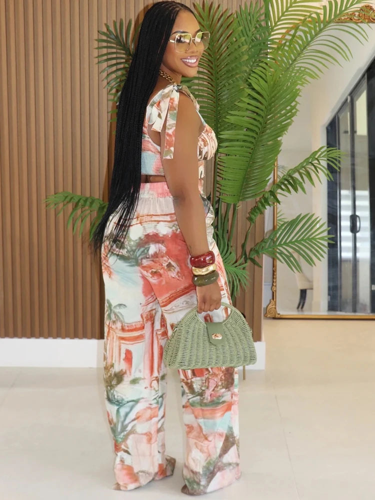 Woman wearing a colorful two-piece outfit with a cropped tied top and wide-leg pants, holding a green handbag indoors