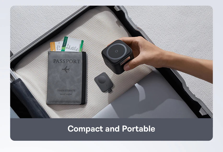 Hand placing a compact black wireless magnetic charger inside an open suitcase next to a passport and travel documents