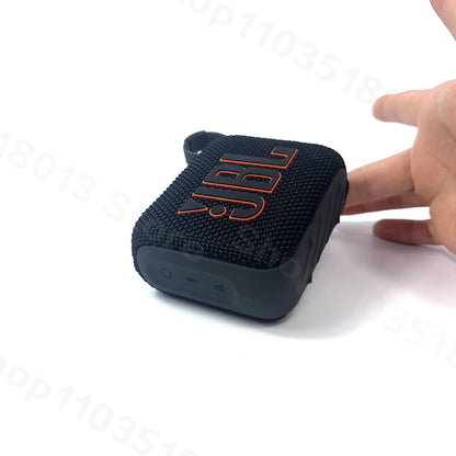 Hand holding compact black JBL GO 4 portable waterproof Bluetooth speaker with textured fabric surface on white background