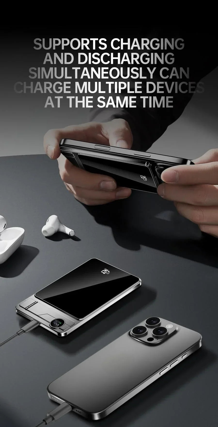 Person holding a smartphone above a wireless power bank charging multiple devices on a dark surface with earbuds nearby