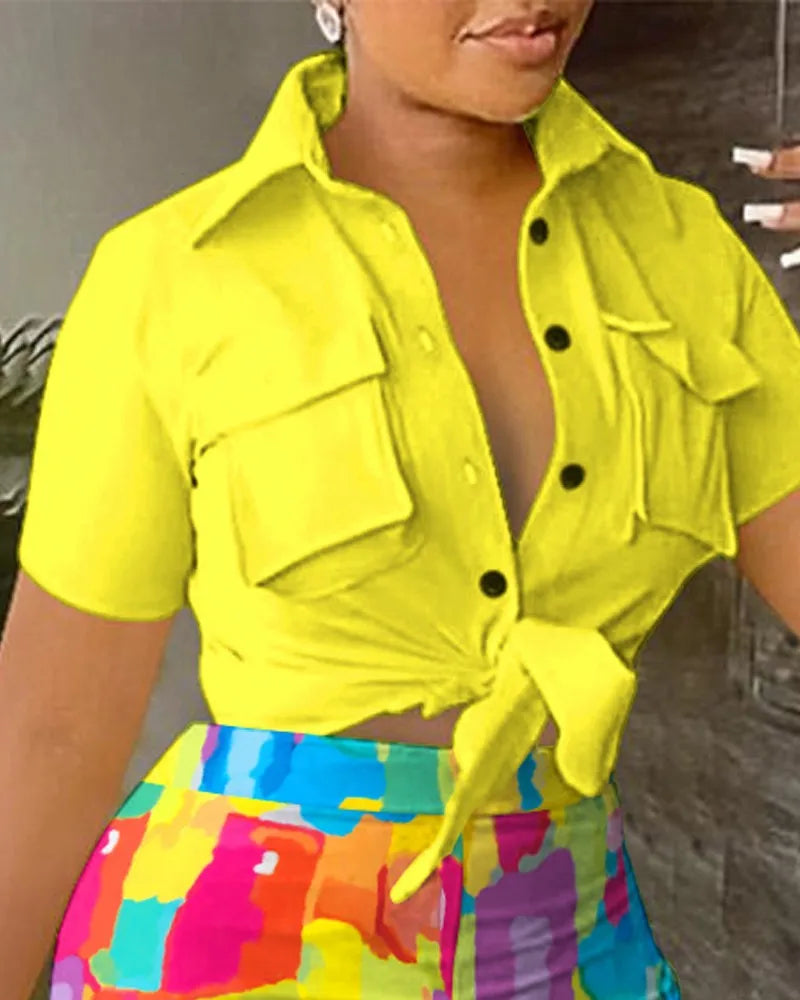 Woman wearing a yellow short-sleeve button-up tied crop top and colorful high-waisted shorts with abstract print