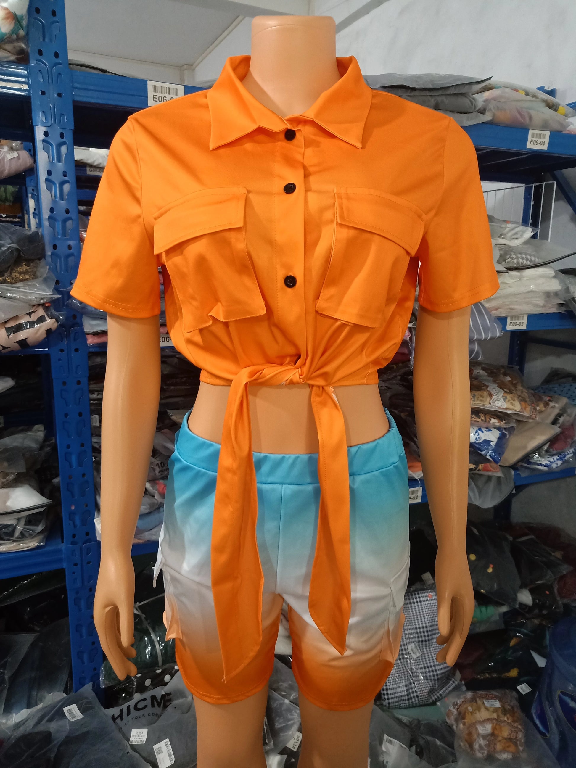 Female mannequin wearing an orange short-sleeve tie-front blouse and blue-to-orange ombre shorts two-piece summer outfit