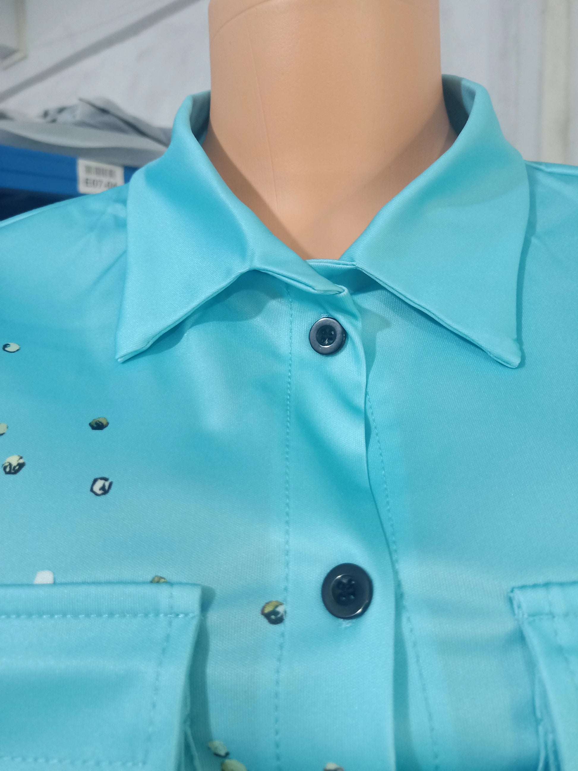 Close-up of light blue button-up summer top with collar and subtle printed details on mannequin