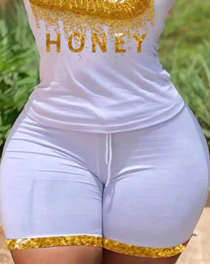 Close-up of a woman wearing a white summer t-shirt and shorts set with gold "Honey" print and trim details.