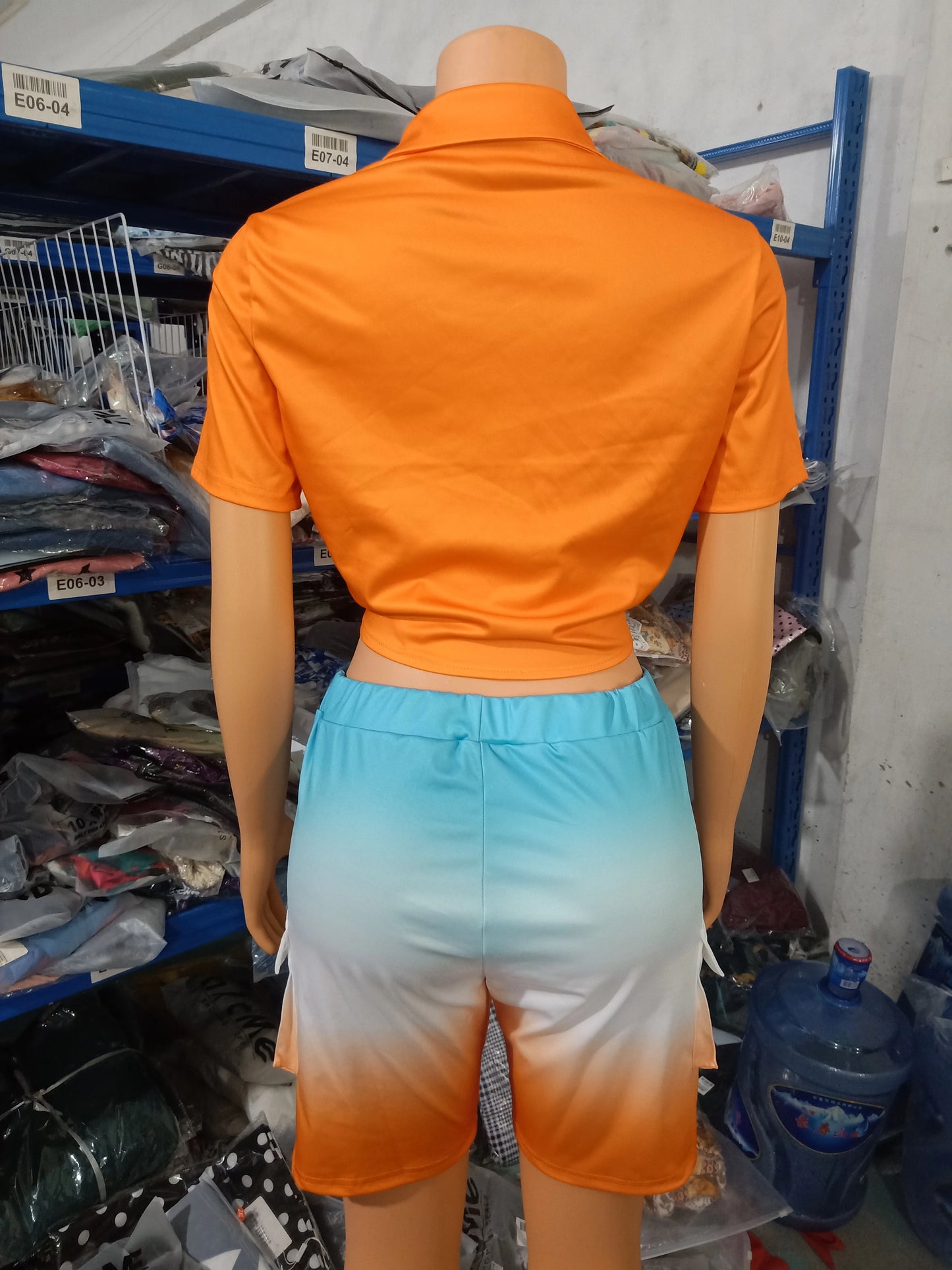 Female mannequin wearing a short-sleeve orange cropped top and ombre blue to orange shorts two-piece summer outfit