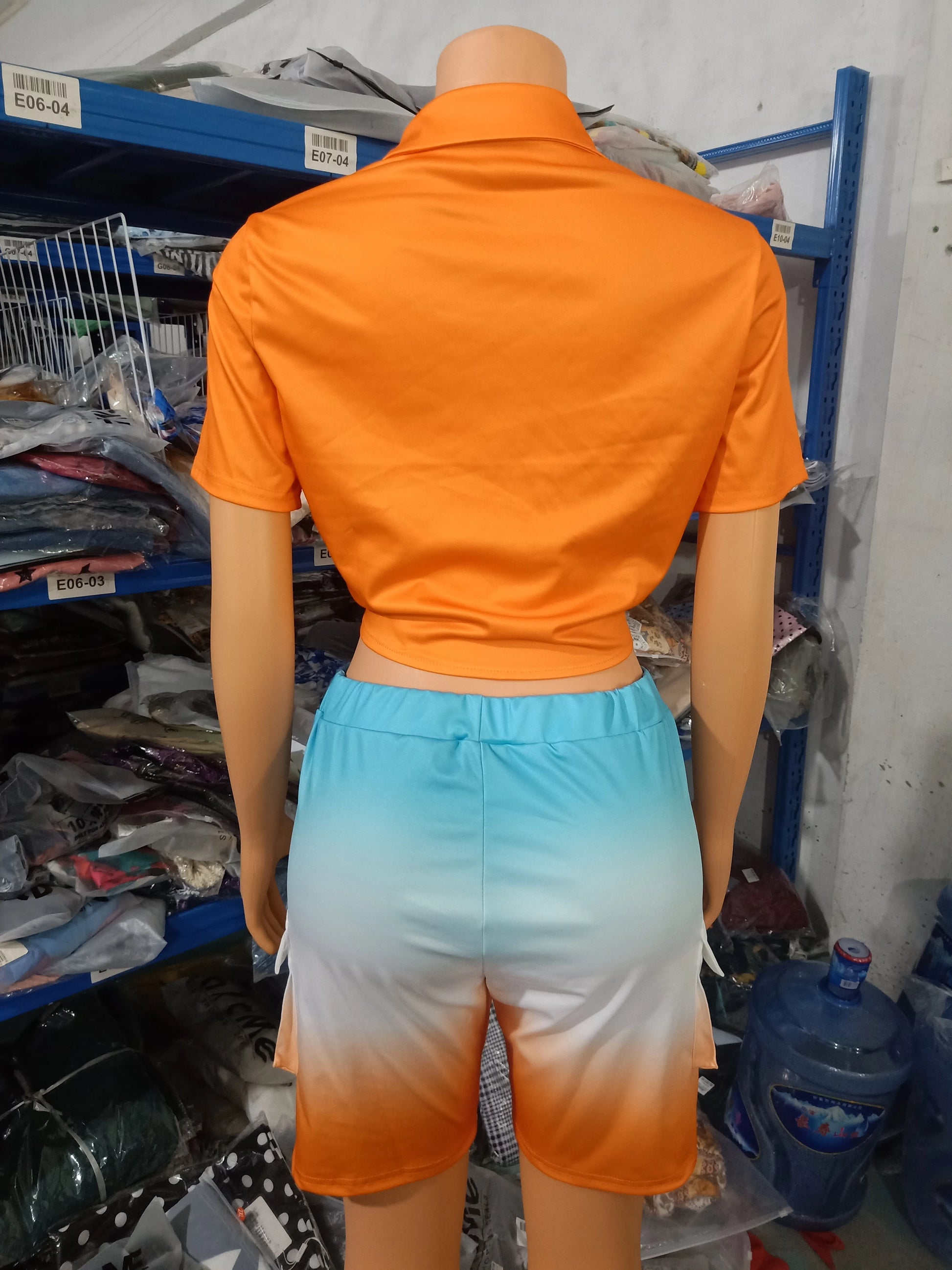 Female mannequin wearing a short-sleeve orange cropped top and ombre blue to orange shorts two-piece summer outfit