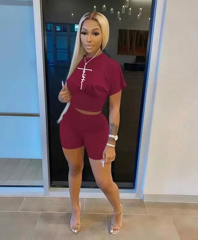 Woman wearing a fitted maroon two-piece outfit with a cropped t-shirt and high-waisted shorts indoors