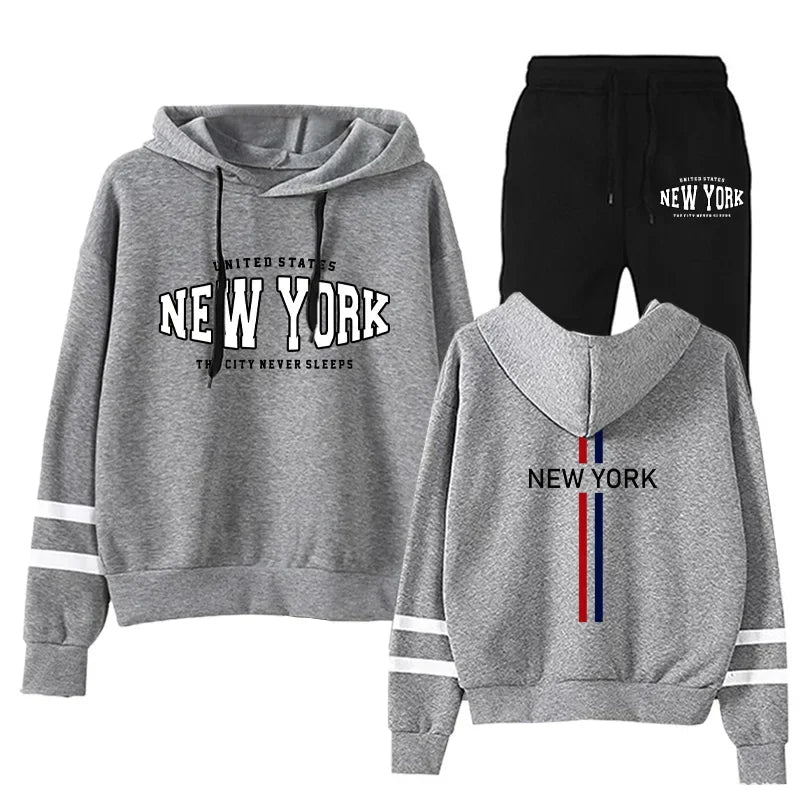 Women's two-piece jogging set with grey hoodie featuring New York print and black drawstring pants with stripe details