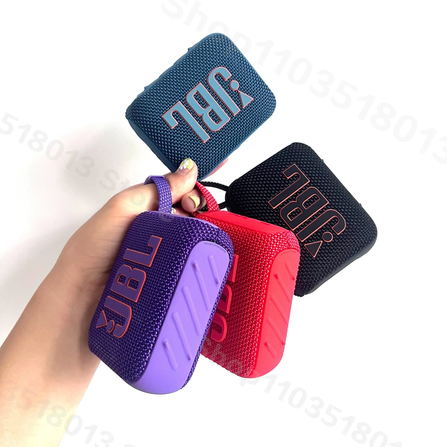 Hand holding four portable JBL GO 4 Bluetooth wireless speakers in blue, black, red, and purple colors on a white background