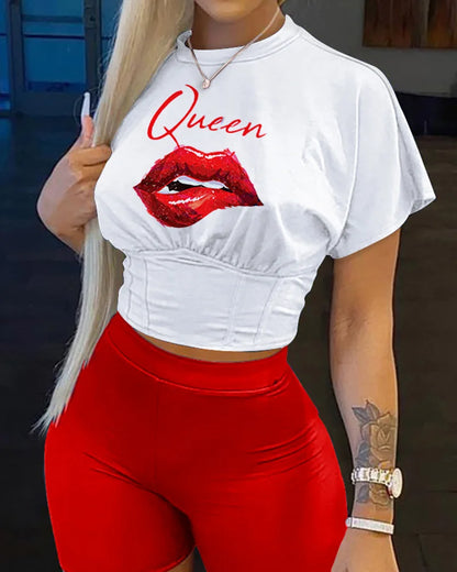 Woman wearing white cropped Queen t-shirt with red lips print and high-waisted red shorts against dark background