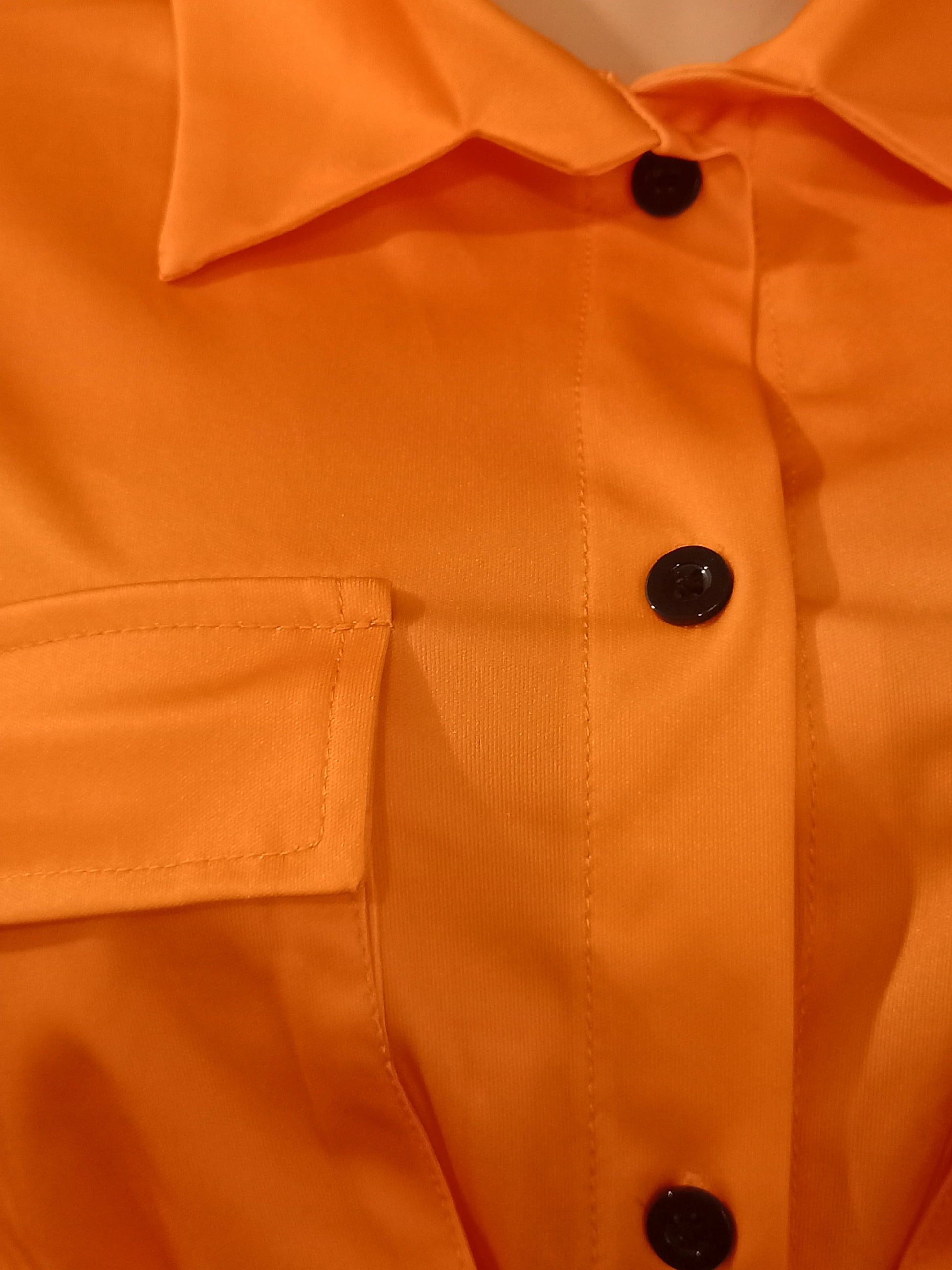 Close-up of an orange short-sleeve shirt with black buttons and a chest pocket detail from summer two-piece set