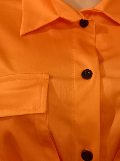 Close-up of an orange short-sleeve shirt with black buttons and a chest pocket detail from summer two-piece set