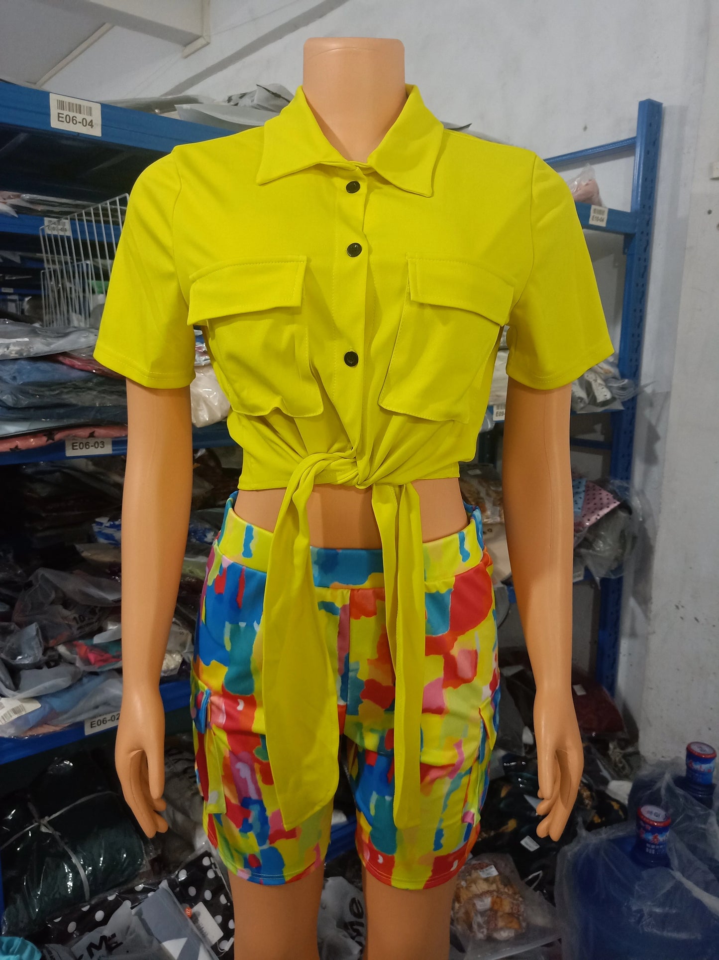 Female mannequin wearing a bright yellow tied crop top with front pockets and colorful patterned shorts summer outfit