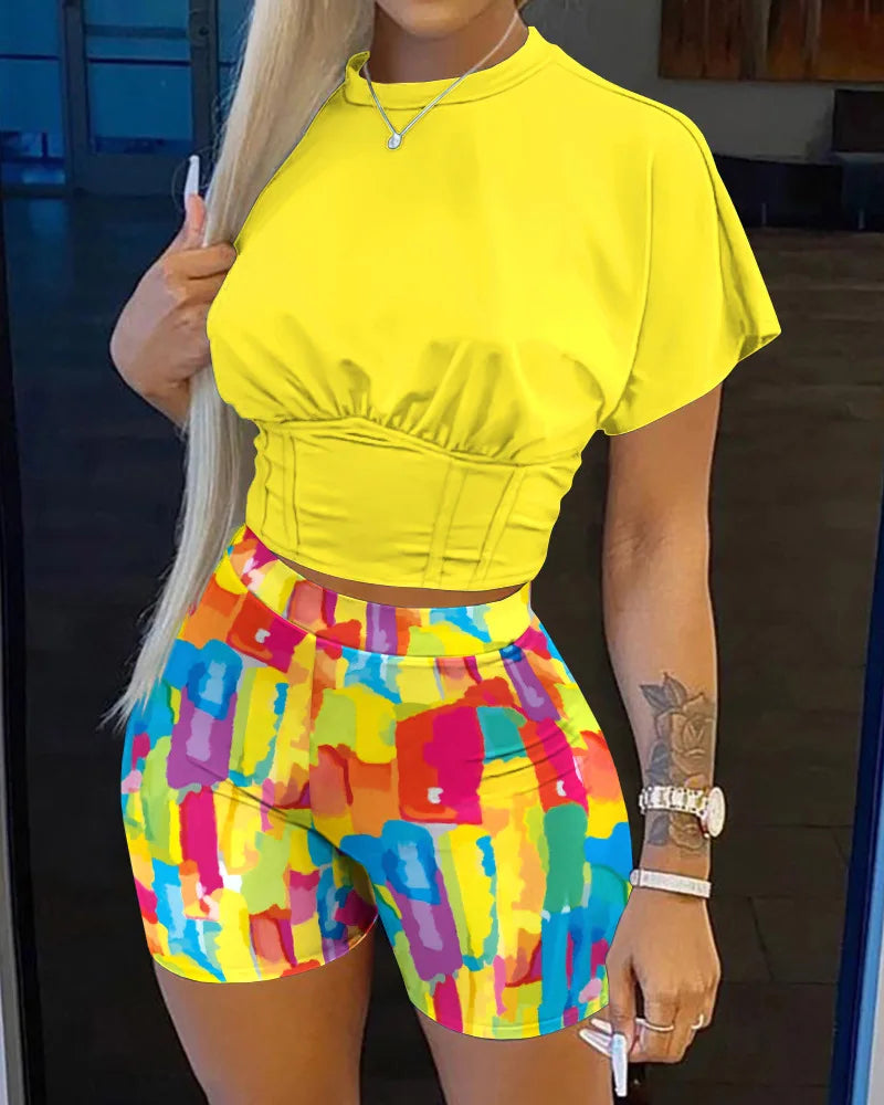 Woman wearing a bright yellow cropped top and colorful abstract print shorts in a casual summer outfit