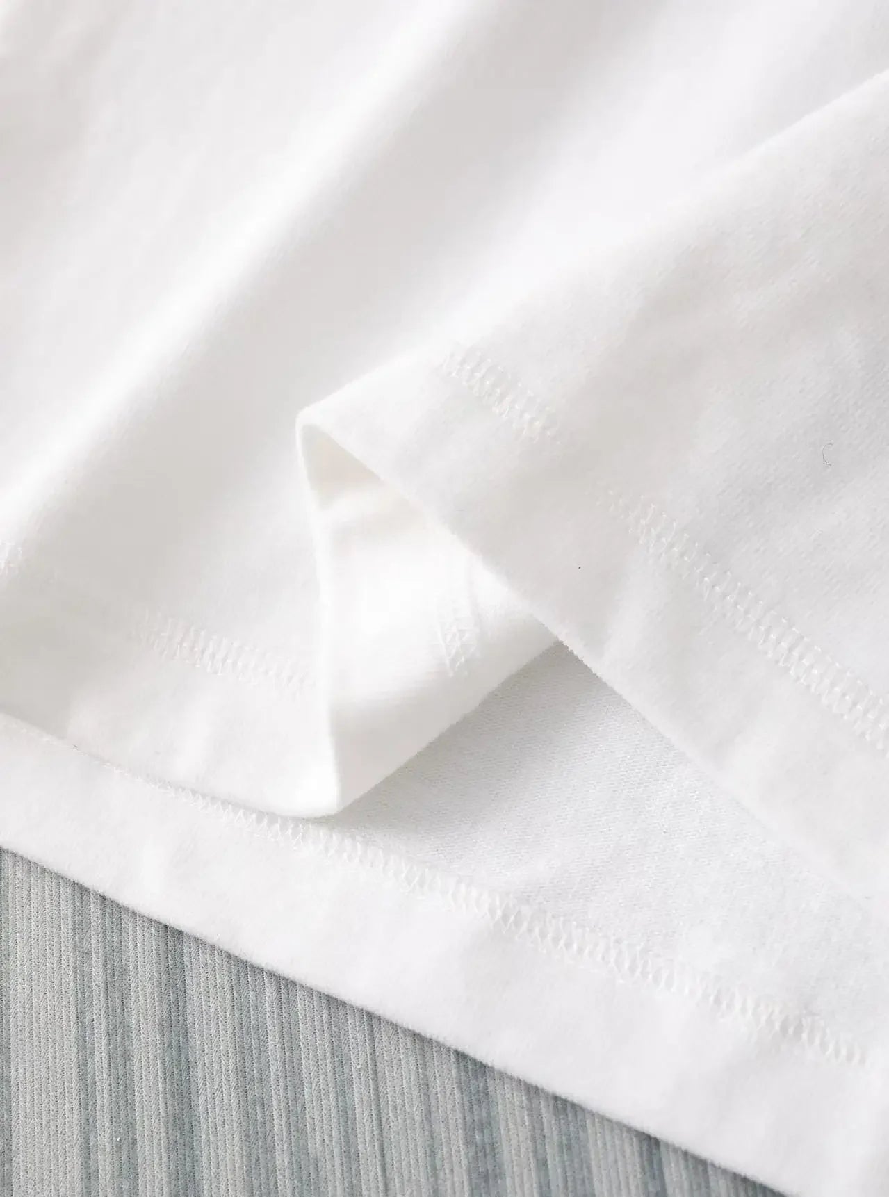 Close-up of white Harajuku artistic streetwear t-shirt fabric and stitching details on hem