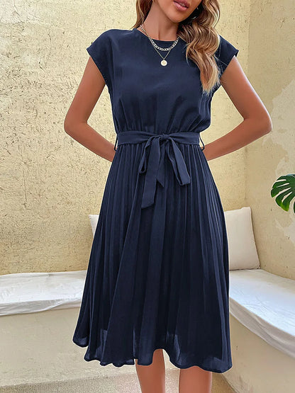 Elegant navy blue pleated summer beach dress for women with cap sleeves and waist tie belt on neutral background