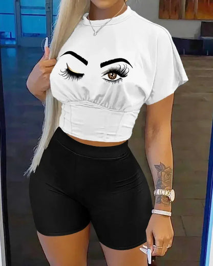 Woman wearing a white crop top with winking eye graphic and fitted high-waisted black shorts two-piece outfit