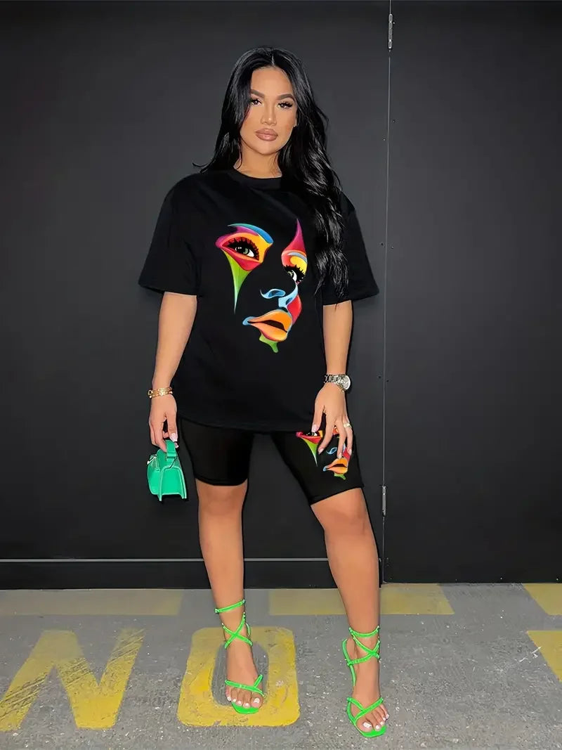 Woman wearing a black two-piece set with a colorful face graphic t-shirt and matching skinny shorts holding a green handbag