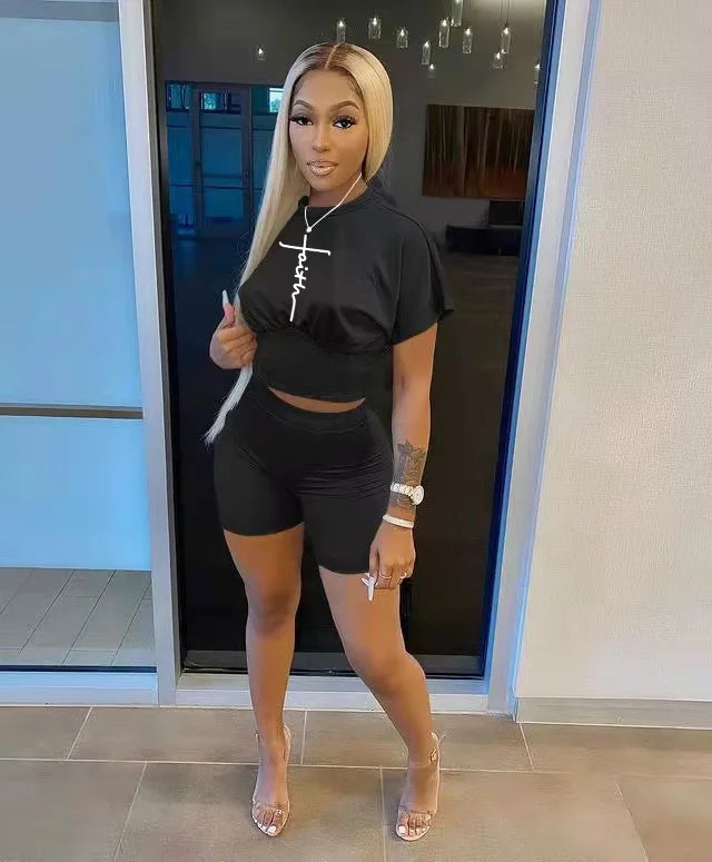 Woman wearing a black two-piece summer outfit with a fitted t-shirt and high-waisted shorts indoors