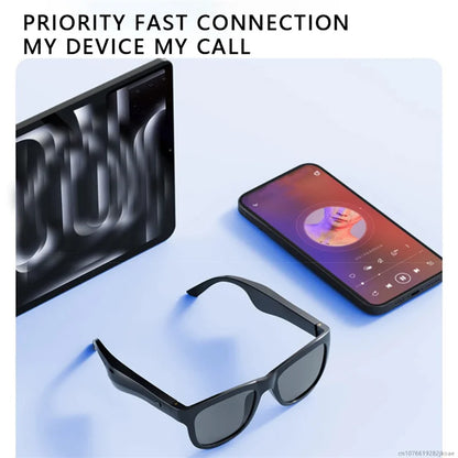 Black smart sunglasses with built-in earbuds placed near a smartphone and tablet on a light surface