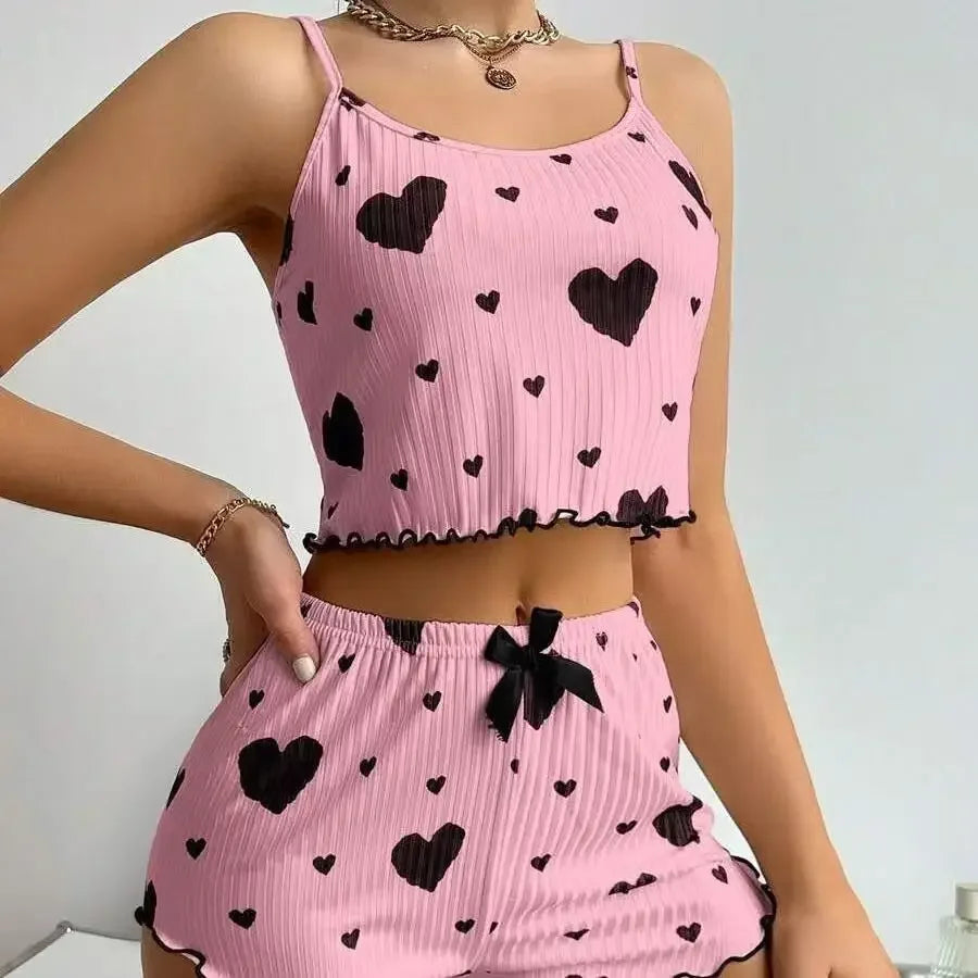 Woman wearing a pink two-piece pajama set with black heart prints, featuring a crop top and matching shorts with bow detail