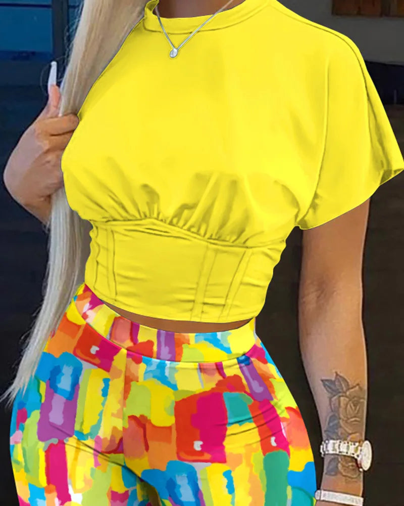 Woman wearing a bright yellow fitted crop top with colorful abstract pattern pants, showcasing summer fashion style.