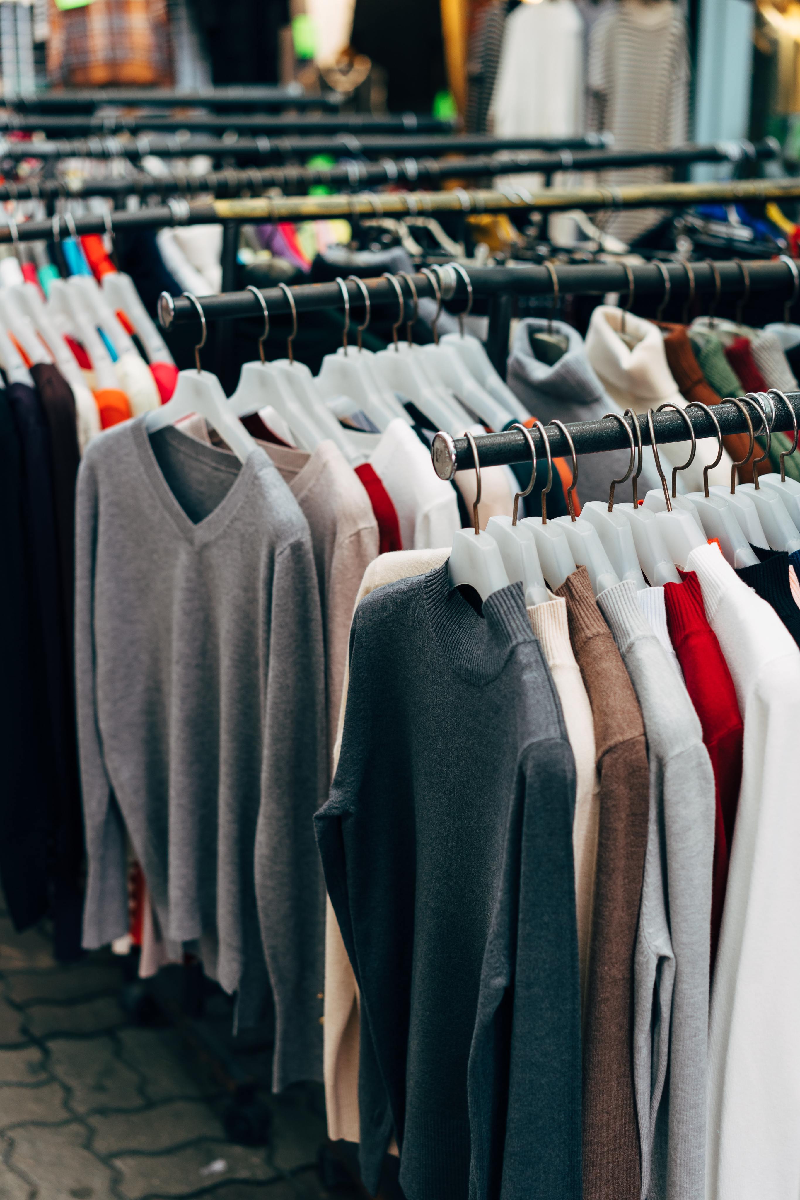 Row of hanging sweaters in various neutral and muted colors displayed on black racks in a clothing store.