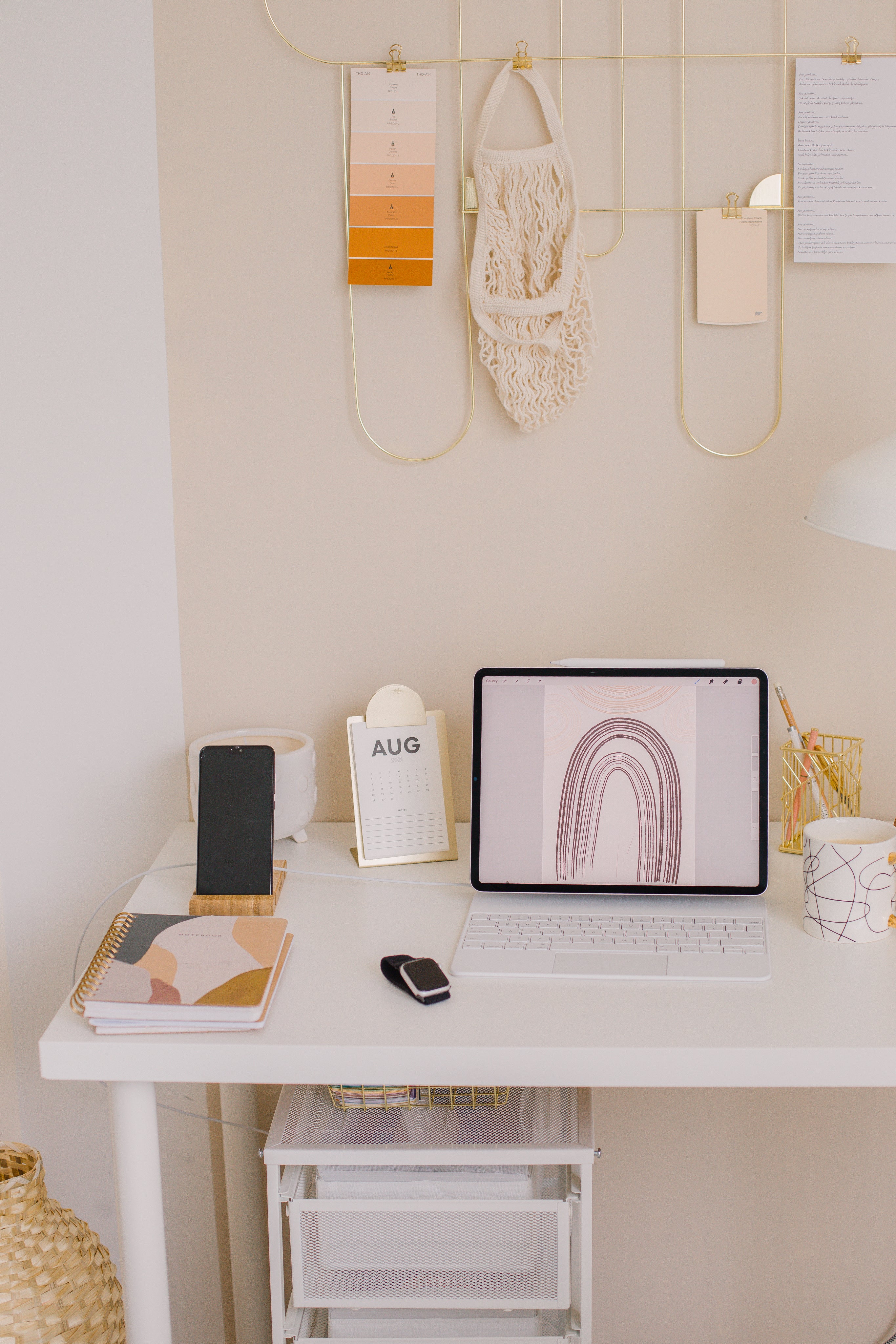 Minimalist workspace with tablet, smartphone, notebook, and calendar on white desk against beige wall